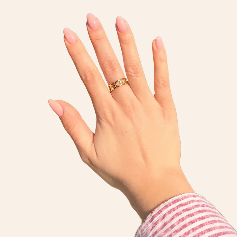 Main portant la bague Chicago dorée en acier inoxydable, bijou raffiné avec maillons entrelacés créant un effet sophistiqué.