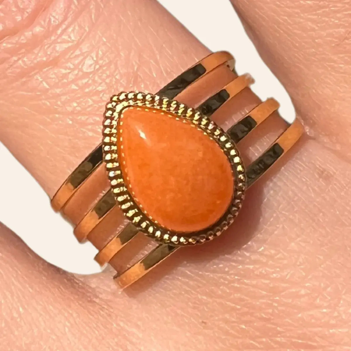 Gros plan sur la bague Jaipur dorée avec goutte orange, soulignant la brillance de la goutte et le design chic.