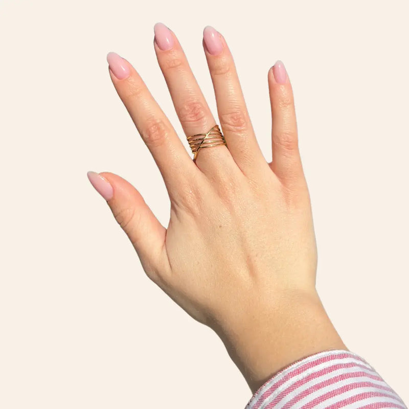 Main portant la bague La Valette dorée en acier inoxydable, bijou tendance à traits croisés élégants.