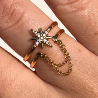 Zoom sur la bague Londres dorée en acier inoxydable, mettant en valeur l’étoile ornée de strass et la chaîne suspendue, créant un effet élégant et avant-gardiste.
