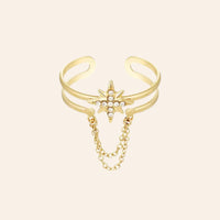 Bague Londres en acier inoxydable doré, étoile ornée de strass scintillants avec chaîne suspendue, capturant l'audace et le style avant-gardiste de Londres, présentée seule sur fond neutre.