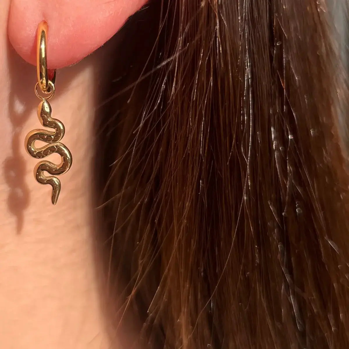 Boucles Jakarta dorées portées, bijou élégant avec serpent suspendu, ajoutant une touche audacieuse et contemporaine.