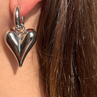 Boucles Prague en acier inoxydable argenté portées, gros cœur suspendu, ajoutant une touche de douceur et de sophistication.