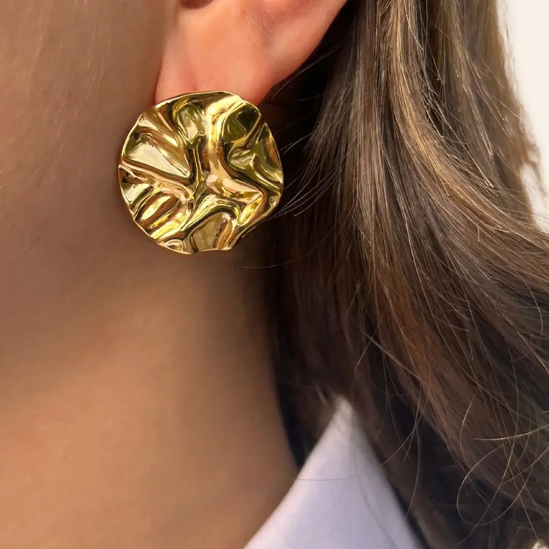 Boucles d’oreilles Berlin dorées portées, surface texturée et design structuré capturant subtilement la lumière et créant un jeu d’ombres élégant.