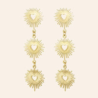 Boucles d'oreilles Dubaï en acier inoxydable doré, pendentifs solaires sculptés et cœurs ajourés, design opulent et moderne, présenté seul sur fond neutre.