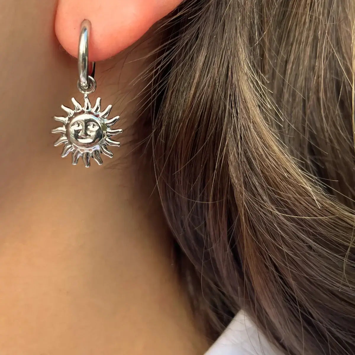 Boucles d’oreilles Madrid en acier inoxydable argenté portées, pendants soleils rayonnants, évoquant la chaleur et la lumière de la capitale espagnole.