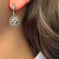 Boucles d’oreilles Madrid en acier inoxydable argenté portées, pendants soleils rayonnants, évoquant la chaleur et la lumière de la capitale espagnole.