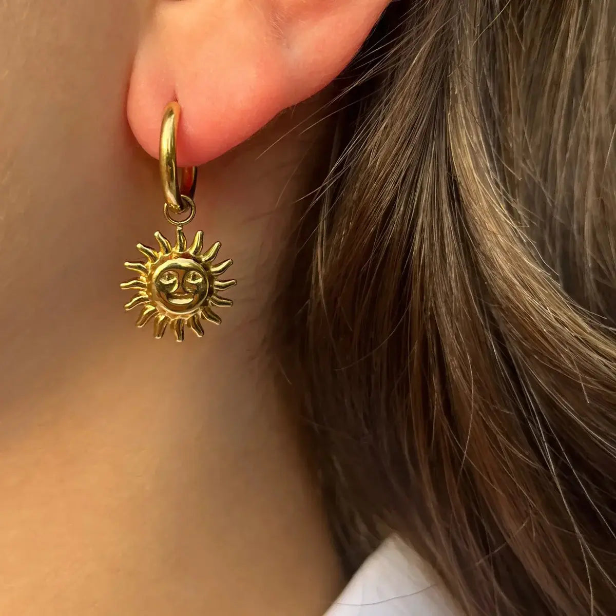 Boucles d’oreilles Madrid dorées portées, design délicat avec pendants de soleils rayonnants, inspiré de la lumière dorée des rues animées de Madrid.
