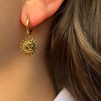 Boucles d’oreilles Madrid dorées portées, design délicat avec pendants de soleils rayonnants, inspiré de la lumière dorée des rues animées de Madrid.