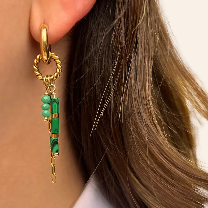 Boucles d’oreilles Mexico dorées portées, créole lisse avec anneau torsadé et perles vertes accompagnées de pierres allongées, combinant élégance et vivacité dans un style inspiré de Mexico.