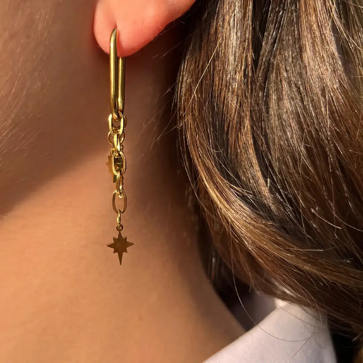 Boucles d’oreilles Oslo dorées portées, pendentifs étoilés suspendus à des chaînes fines, symbolisant la pureté et la clarté des cieux scandinaves.