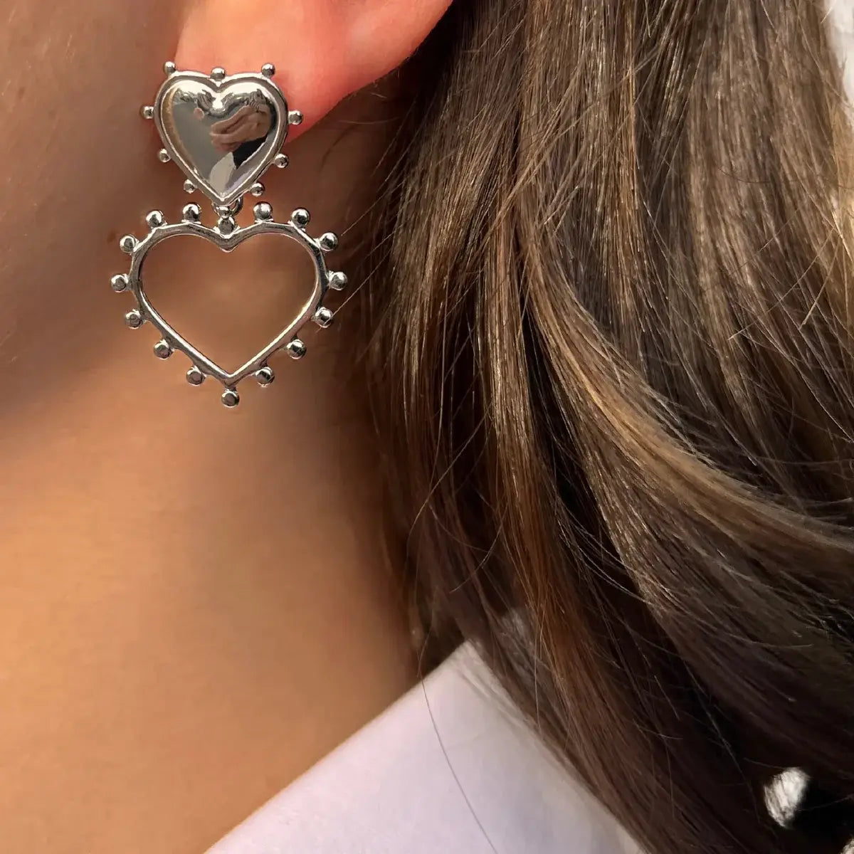 Boucles d’oreilles Paris en acier inoxydable argenté portées, design en deux cœurs, l'un plein et l'autre ouvert, avec des perles délicates pour un look doux et élégant.