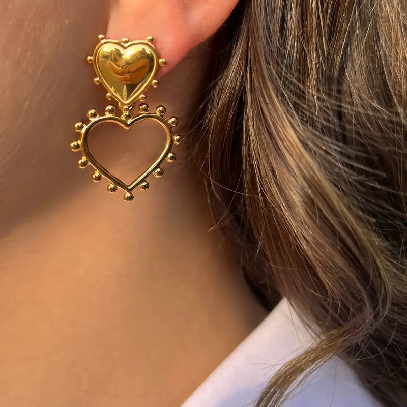 Boucles d’oreilles Paris dorées portées, deux cœurs superposés, l'un plein et l'autre ouvert, sublimés de perles délicates pour une touche de féminité et d’élégance.