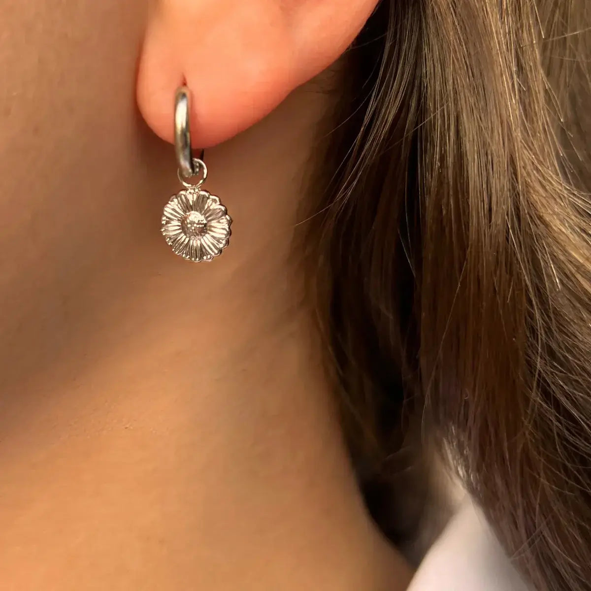Boucles d’oreilles Pretoria en acier inoxydable argenté portées, petite fleur suspendue ajoutant une touche de raffinement et de douceur à votre visage.