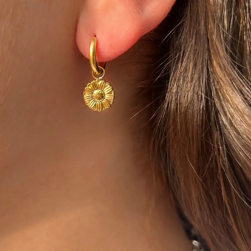 Boucles d’oreilles Pretoria dorées portées, petite fleur suspendue symbolisant l’élégance et la tranquillité, ajoutant une touche subtile à votre look.