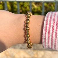 Poignet féminin portant le bracelet Grenade doré, bijou élégant avec des perles dorées ajoutant une touche sophistiquée.