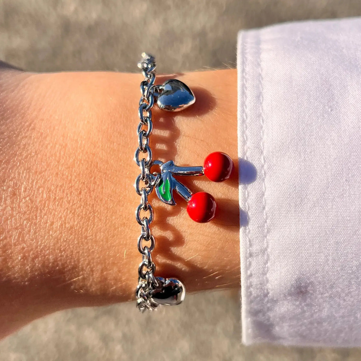 Bracelet Lisbonne en acier inoxydable argenté porté, ajoutant une touche de douceur et de fraîcheur avec ses charms cœurs et cerise.