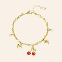 Bracelet Lisbonne en acier inoxydable doré, charm délicat avec deux petits cœurs et pendentif cerise rouge vif, présenté seul sur fond neutre.