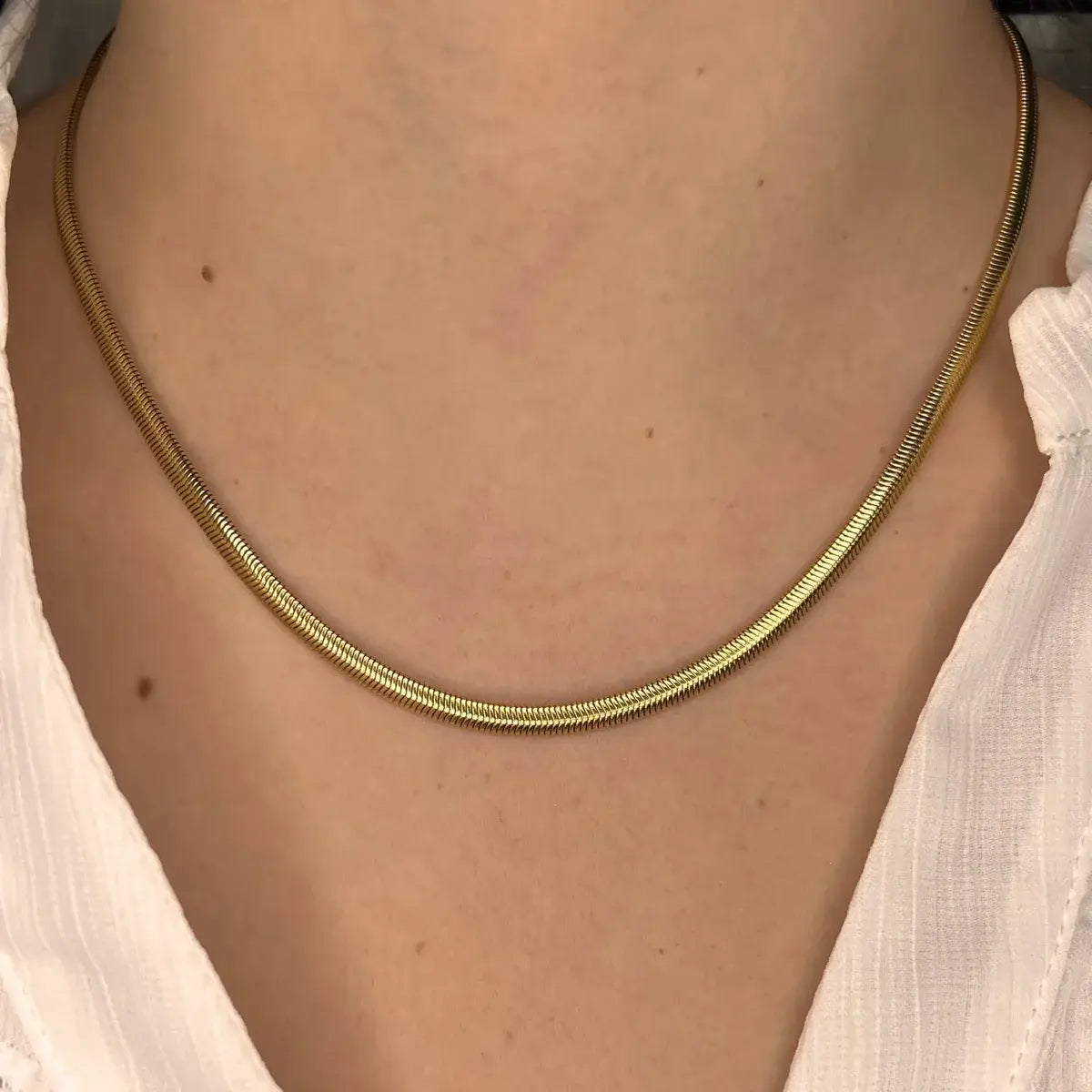 Collier Brasilia doré porté, chaîne délicate reposant élégamment sur le cou, parfait pour un look minimaliste et raffiné.