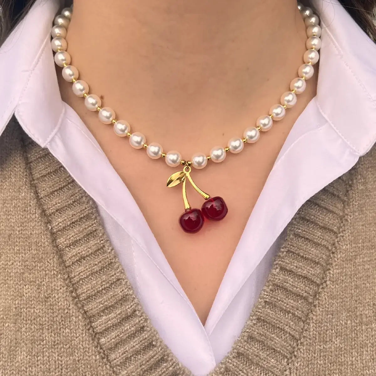 Collier Lisbonne doré porté, perles délicates et pendentif cerise ajoutant une touche de fraîcheur et de joie de vivre à votre look.