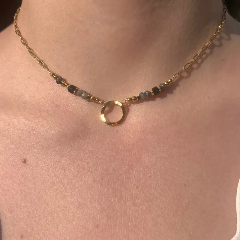 Collier Zanzibar doré et noir en acier inoxydable porté en ras de cou, bijou raffiné avec perles foncées et pendentif circulaire.