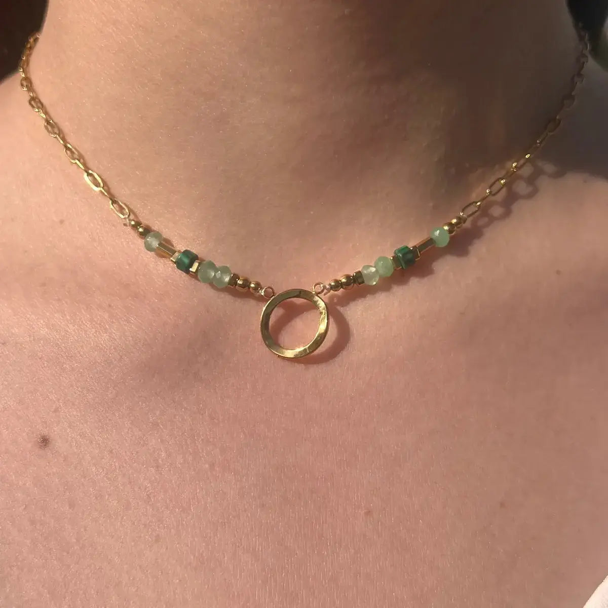 Collier Zanzibar doré et vert en acier inoxydable porté en ras de cou, orné de perles et d’un pendentif rond central.
