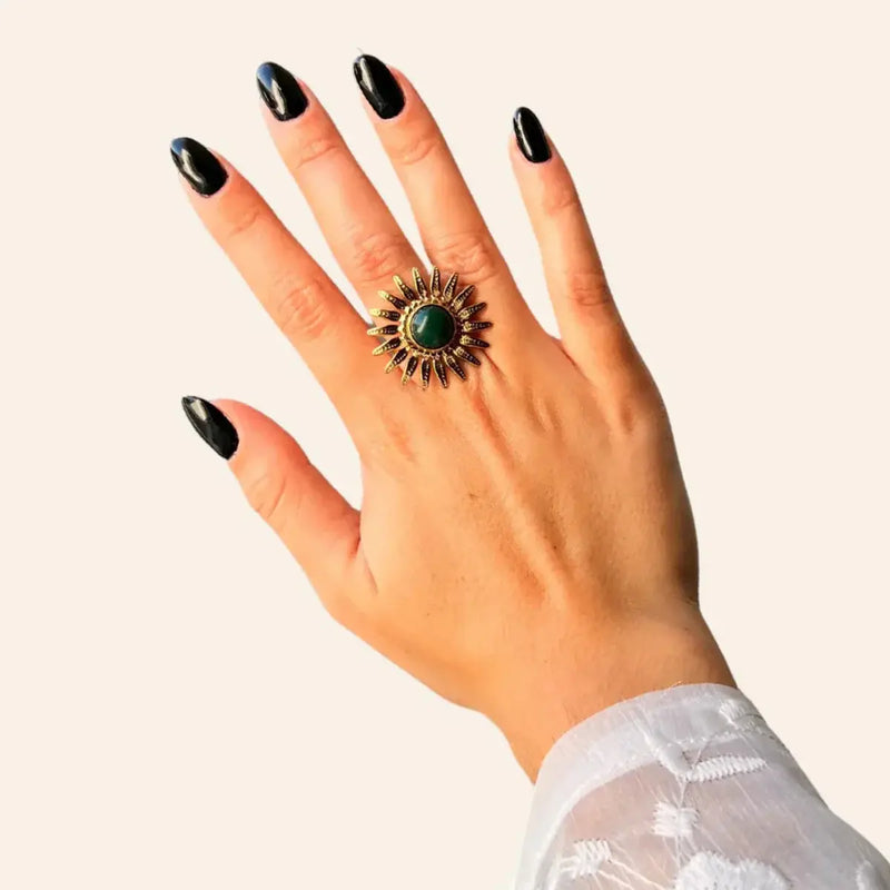 Bague Dakar dorée portée, pierre centrale en vert entourée de rayons dorés, symbolisant la chaleur et la vivacité de Dakar, où tradition et modernité se rencontrent.