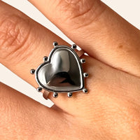 Gros plan sur la bague Paris argentée, détaillant le cœur sculpté et les éléments raffinés, capturant la romance et la beauté intemporelle de Paris.