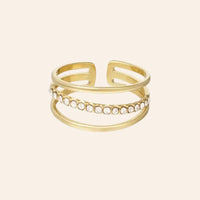 Bague Vienne en acier inoxydable doré, trois anneaux superposés, avec l'anneau central orné de strass scintillants, capturant l’élégance impériale et la sophistication de Vienne, présentée seule sur fond neutre.