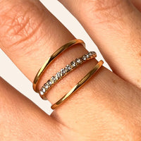 Zoom sur la bague Vienne dorée en acier inoxydable, mettant en valeur l'anneau central orné de strass scintillants, entouré de deux anneaux délicats.