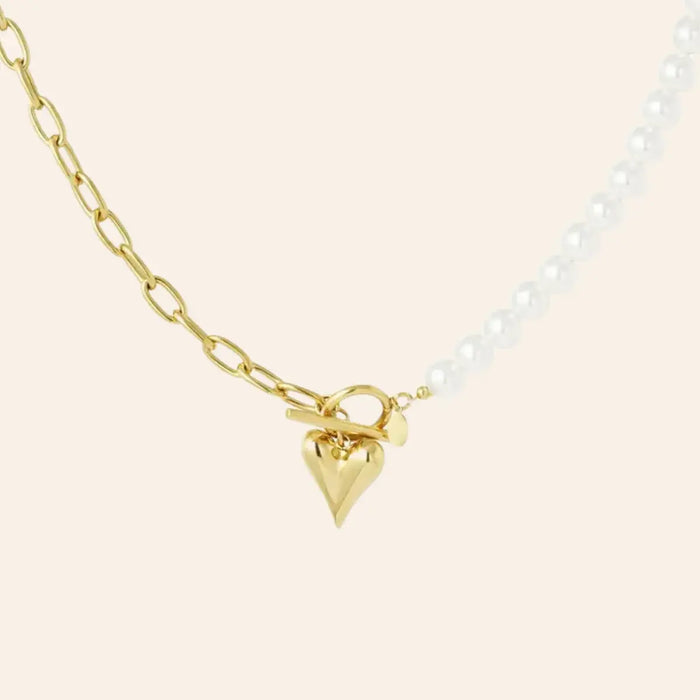 Collier Prague en acier inoxydable doré, moitié chaîne de maillons modernes, moitié perles délicates, orné d'un charm cœur suspendu, présenté seul sur fond neutre.