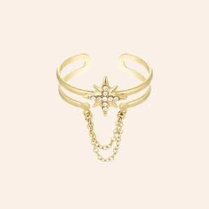 Bague Londres en acier inoxydable doré, étoile ornée de strass scintillants avec chaîne suspendue, capturant l'audace et le style avant-gardiste de Londres, présentée seule sur fond neutre.