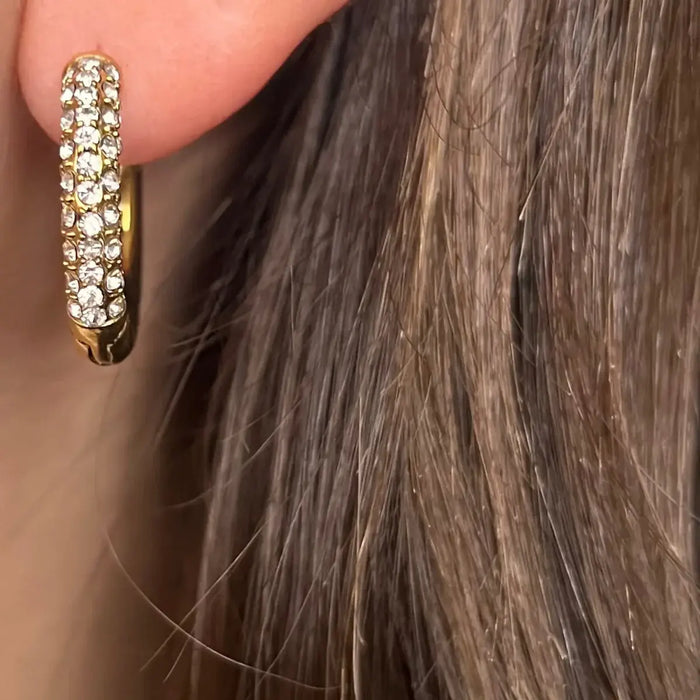 Boucles d’oreilles Milan dorées portées, créoles sophistiquées avec strass blancs, ajoutant une touche de raffinement à votre look.